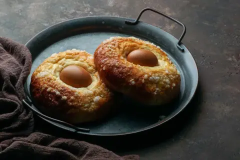 Dos monas de Pascua esponjosas, cubiertas de azúcar, con un huevo cocido incrustado en cada una, listas para disfrutar.
