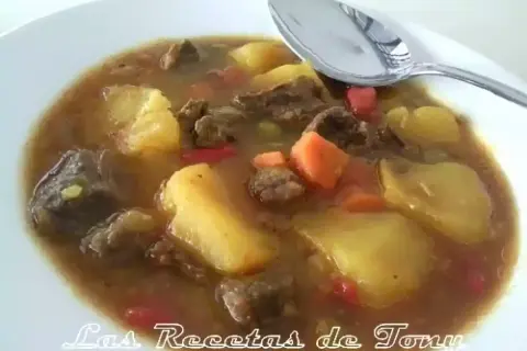 Un plato humeante de patatas con carne olla express, con trozos de zanahoria y pimiento rojo.