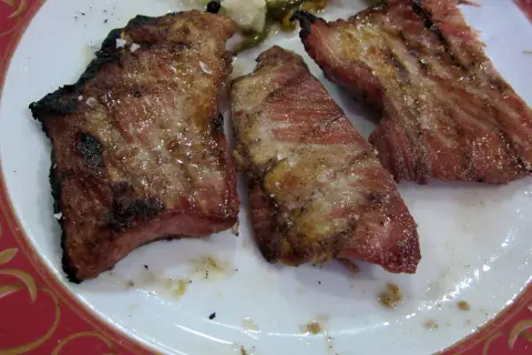 Tres jugosas porciones de secreto ibérico a la parrilla, con sal gruesa y un toque de pimienta, servidas en un plato blanco con borde rojo.