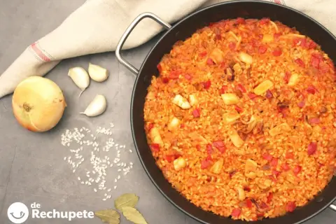 Paella de arroz con calamares, pimientos rojos y especias. Ingredientes frescos como cebolla y ajos acompañan este delicioso plato.