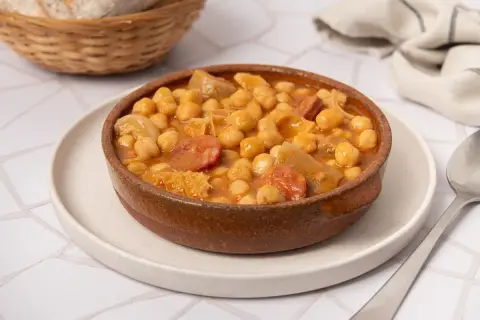 Un plato humeante de callos con garbanzos, chorizo y trozos de carne, servido en una cazuela de barro.