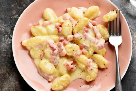 Ñoquis a la carbonara cremosos y deliciosos, cubiertos con trozos de panceta y pimienta negra, servidos en un plato rosa.