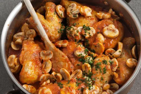 Pollo con gambas y champiñones en salsa roja, servido en una olla de metal con una cuchara de madera.