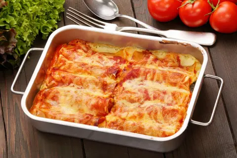 Canelones de atún gratinados en una bandeja metálica, listos para servir. Acompañados de tomates frescos y lechuga.