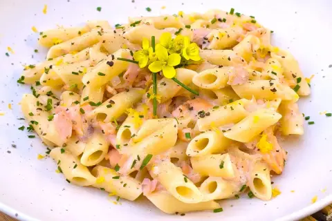 Pasta penne cremosa con trozos de salmón rosado, ralladura de limón y flores amarillas. Un plato delicioso.