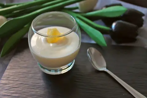 Delicioso postre de lemon curd en copa, decorado con un trozo de limón. Una cuchara plateada y tulipanes negros completan la escena.