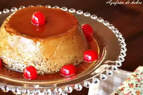 Delicioso flan de café con caramelo líquido y cerezas rojas, servido en un plato de cristal decorado.