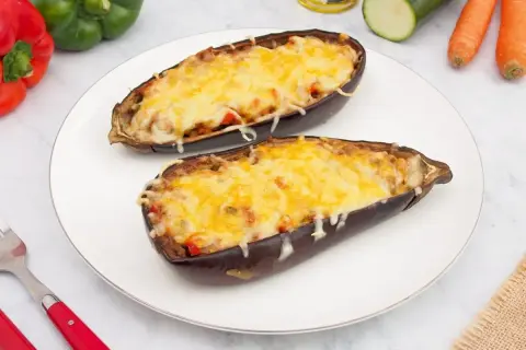Dos mitades de berenjenas rellenas de verduras y cubiertas de queso gratinado, listas para disfrutar.
