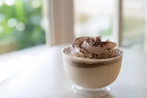Delicioso mousse de café con crema batida y cacao espolvoreado, servido en un vaso transparente.