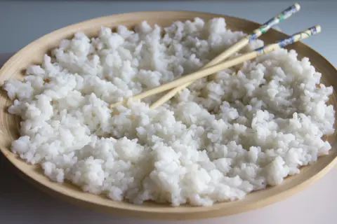 Arroz para sushi listo para preparar tus makis favoritos. Palillos cruzados sobre el arroz blanco y pegajoso en un cuenco de madera.
