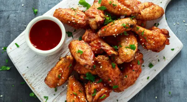 Deliciosas alitas de pollo fritas, doradas y crujientes, servidas con salsa y perejil picado.