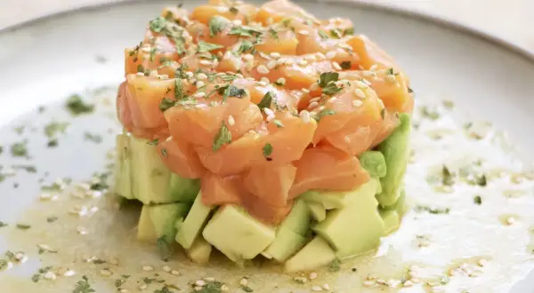 Delicioso tartar de salmón fresco con aguacate, espolvoreado con sésamo y perejil. Una explosión de sabor y color.