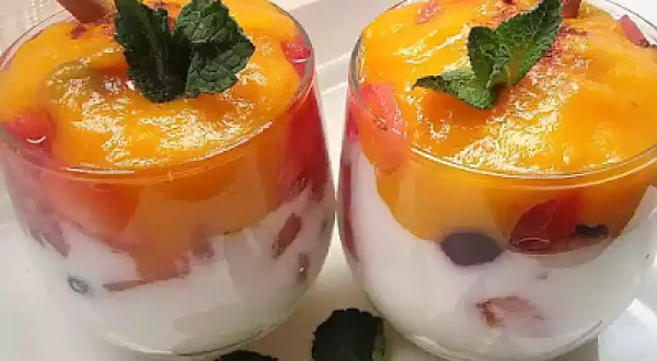 Dos copas de cristal con capas de yogur blanco, trozos de fruta roja y un delicioso mousse de mango coronado con menta y canela.