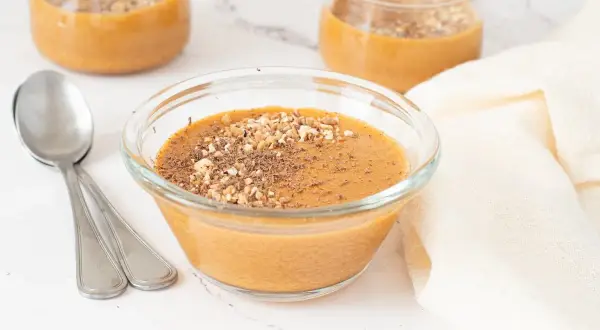 Delicioso postre cremoso, como baba de camelo, servido en un cuenco de cristal con nueces picadas y virutas de chocolate.