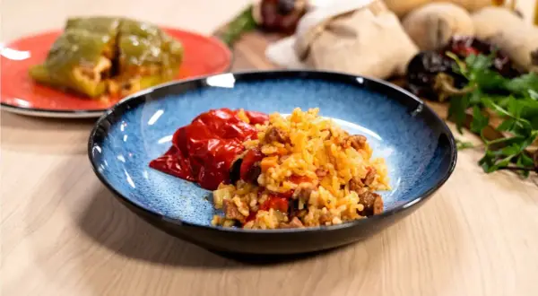 Plato azul con pimientos rellenos de arroz y carne. Otro pimiento verde relleno en un plato rojo al fondo.