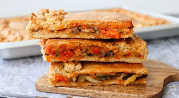 Tres porciones de empanada de verduras apiladas, con relleno de pimientos, calabacín y tomate.