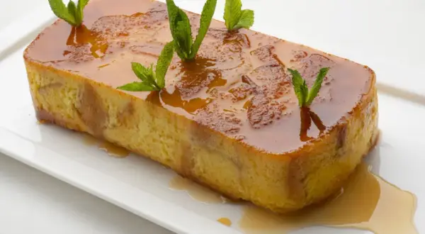Pan de Calatrava, un postre dorado con caramelo líquido y hojas de menta, servido en una bandeja blanca.