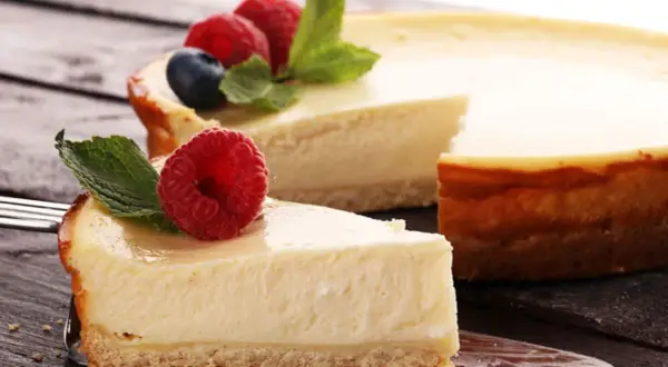 Deliciosa tarta de queso con galletas, coronada con frambuesas frescas y hojas de menta. Un trozo ya servido en un tenedor.