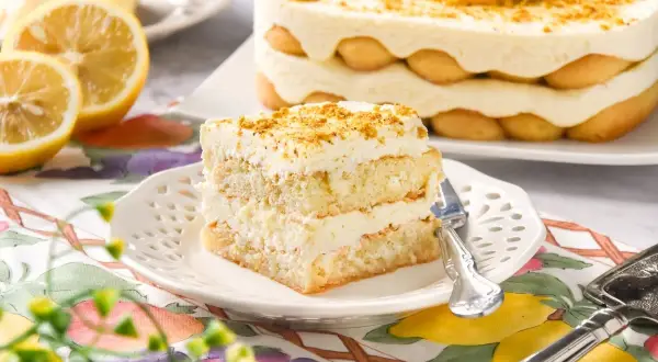 Delicioso tiramisú de limón, con capas de bizcocho, crema y soletillas, decorado con ralladura y rodajas de limón.