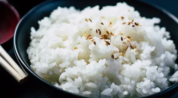 Un tazón de arroz blanco humeante, espolvoreado con semillas de sésamo, listo para ser disfrutado con palillos.