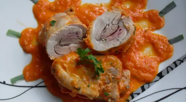 Contramuslos de pollo Thermomix enrollados con jamón, cubiertos de salsa de pimientos y decorados con perejil y cebolleta.