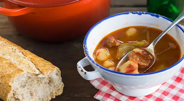 Un reconfortante plato de patatas a la riojana, con chorizo y pimientos, servido en un cuenco blanco con borde azul.