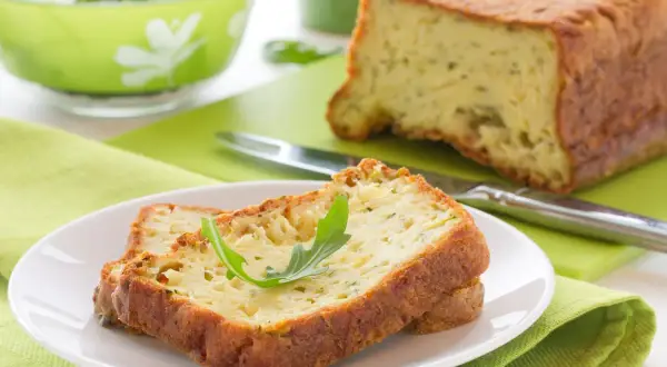 Rebanadas de un delicioso pastel de calabacín, esponjoso y dorado, servidas en un plato blanco con una hoja verde.