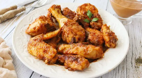 Plato de pollo a la coca cola, jugoso y caramelizado, con un toque de perejil. Servido en una fuente blanca sobre una mesa de madera.