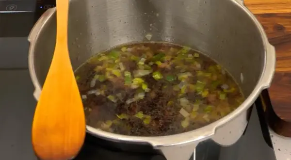 Olla express con alubias y verduras, lista para el tiempo de cocción. Una cuchara de madera descansa a un lado.