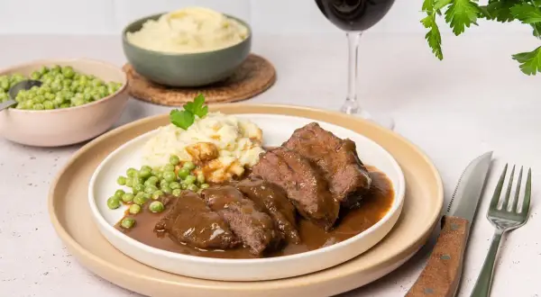 Carrilleras de ternera en salsa, un plato reconfortante que evoca la auténtica receta de la abuela, acompañado de puré de patatas y guisantes.
