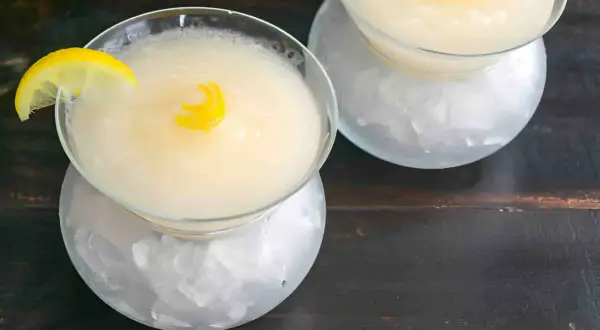 Dos copas de sorbete de limón, una con rodaja y otra con espiral de limón, servidas sobre hielo picado.