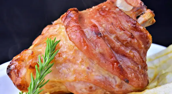 Codillo de cerdo asado, dorado y jugoso, servido con patatas fritas y una ramita de romero.