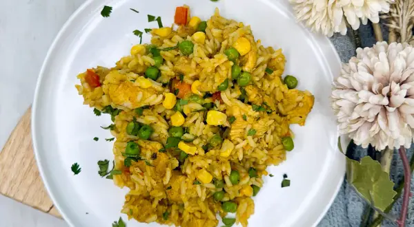 Arroz con pollo de la abuela, un plato casero con pollo tierno, guisantes, maíz y zanahoria, espolvoreado con perejil fresco.