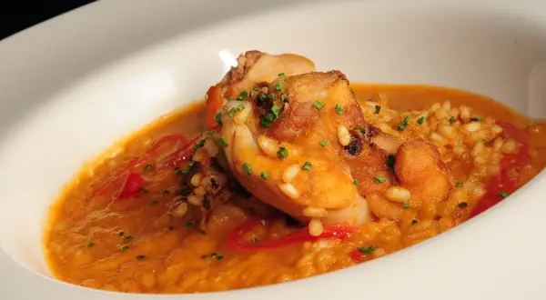 Delicioso arroz con conejo, trozos dorados de carne y pimientos rojos en una cremosa salsa, adornado con cebollino fresco.