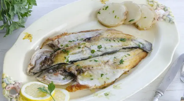 Lubina a la plancha, dorada y jugosa, servida con patatas y rodajas de limón. Un plato sencillo y delicioso.