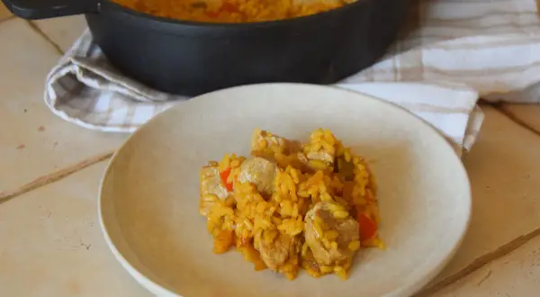 Un plato de arroz con carne, pimientos y trozos de cerdo, servido desde una paellera.