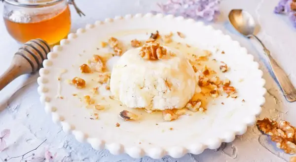 Delicioso postre de mel i mató con nueces y miel, servido en un plato blanco con borde festoneado.