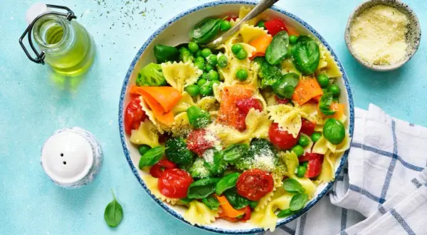 Un plato de pasta con verduras frescas: brócoli, guisantes, tomates cherry y zanahoria, espolvoreado con queso rallado.