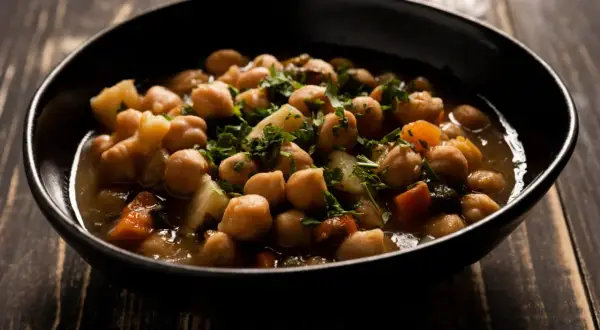 Un tazón de garbanzos con patatas y zanahoria, adornado con perejil fresco. Una deliciosa receta de garbanzos tradicional.