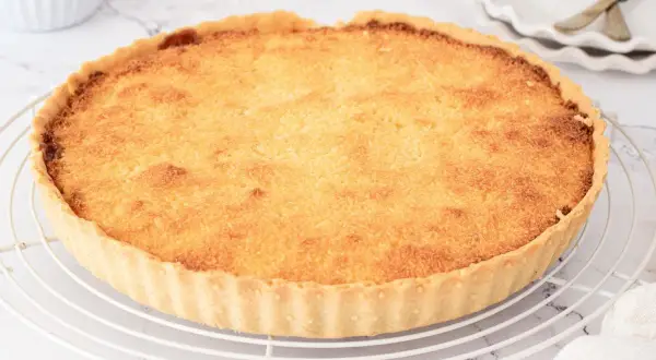 Tarta de coco dorada y crujiente sobre una rejilla. Su relleno esponjoso y aroma tropical invitan a probar esta delicia.