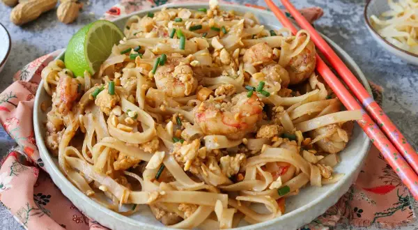 Un delicioso plato de pad thai con camarones, fideos de arroz, cacahuetes picados y cebollino.