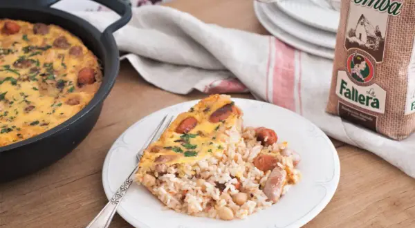 Un delicioso arroz con costra recién hecho, con trozos de salchicha y garbanzos, servido en un plato blanco.