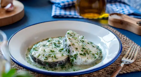 Dos rodajas de merluza en salsa verde, con perejil picado y una cremosa salsa. Un plato casero listo para disfrutar.