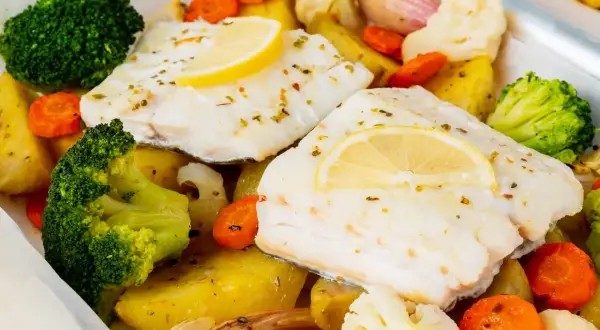 Bacalao al horno con patatas, brócoli, zanahorias y coliflor, todo asado en una bandeja.