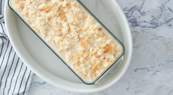 Preparando una deliciosa receta de pudin casero en un molde de vidrio, con trozos de galleta integrados.