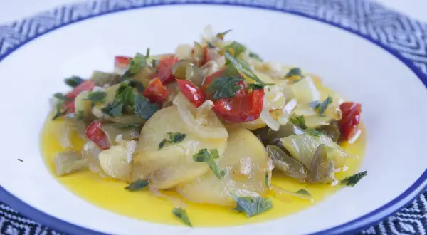 Patatas a lo pobre con pimientos rojos y verdes, cebolla y perejil, servidas en un plato blanco con borde azul.