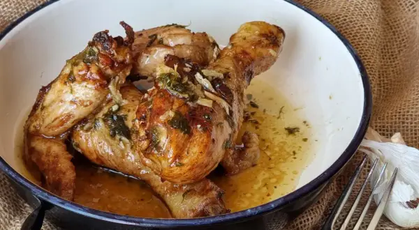 Sabroso pollo al ajillo dorado y jugoso, bañado en su propio jugo con ajo y hierbas, servido en una cazuela.