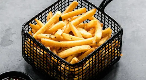 Cesta negra llena de crujientes patatas fritas doradas, listas para ser disfrutadas con una salsa roja.