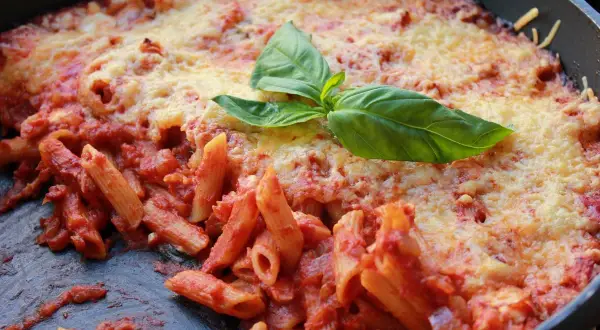 Macarrones al horno con salsa de tomate y queso gratinado, decorados con hojas de albahaca fresca. ¡Un plato casero irresistible!