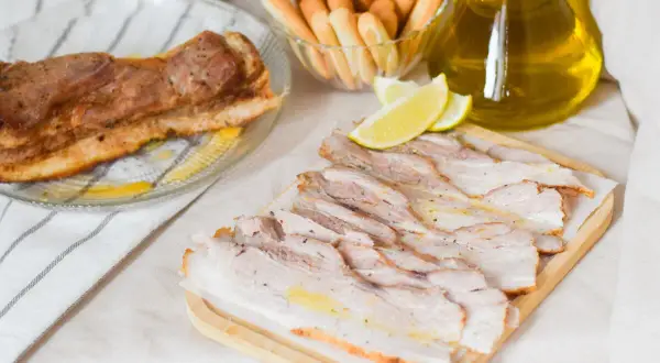 Chicharrón de Cádiz, lonchas de panceta asada, palitos de pan y limón, todo listo para disfrutar.